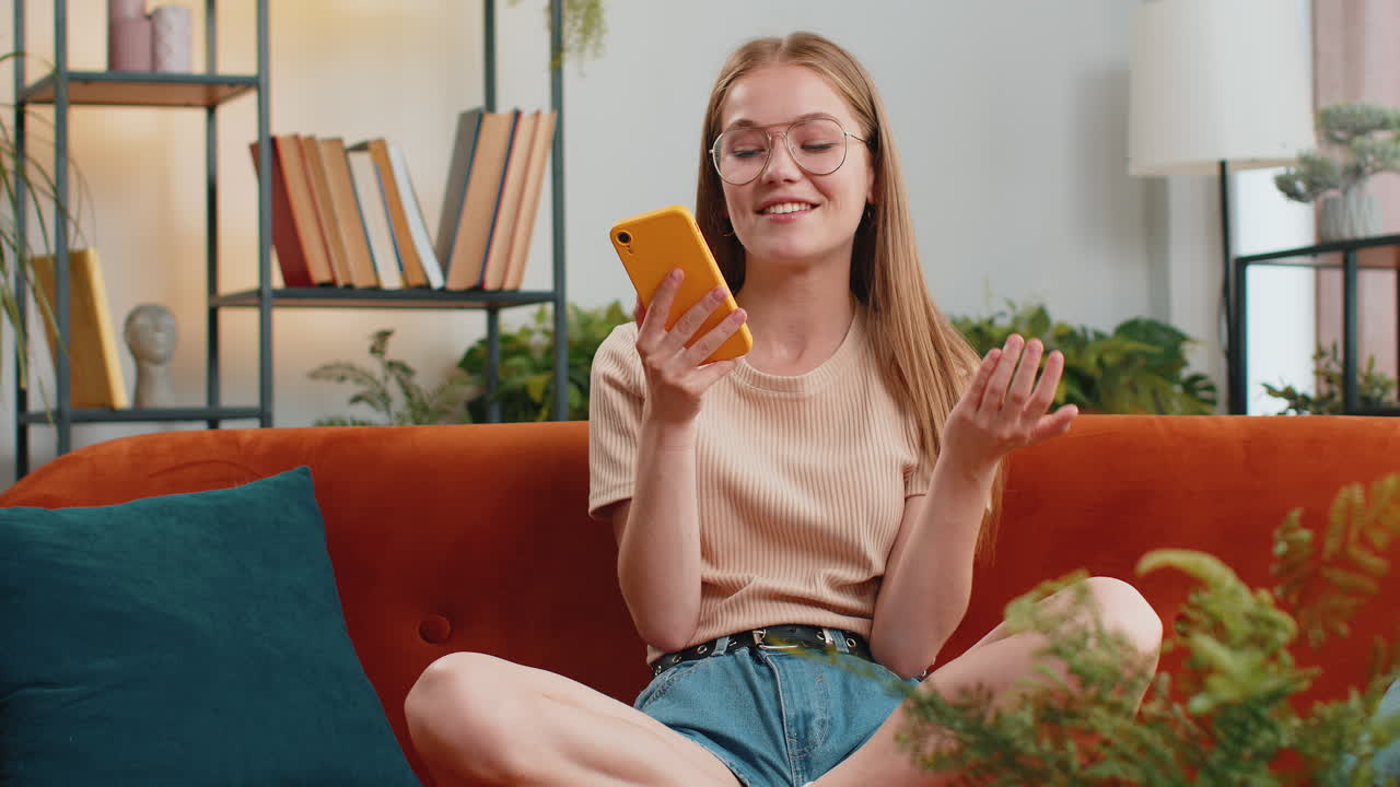 Happy excited young woman making phone call conversation loudspeaker talking with friend at home