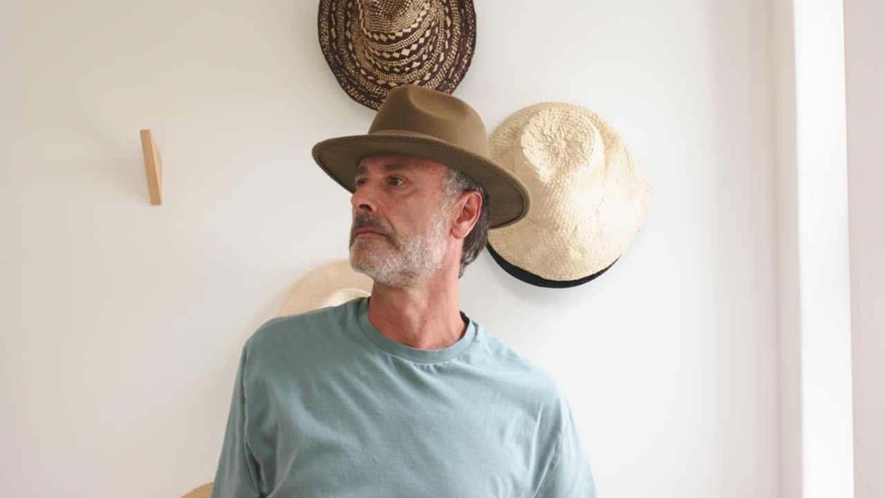 Moden mand tager en brun-grøn fedora fra hatteudstillingen, inspicerer pasformen og justerer hatten på hovedet.