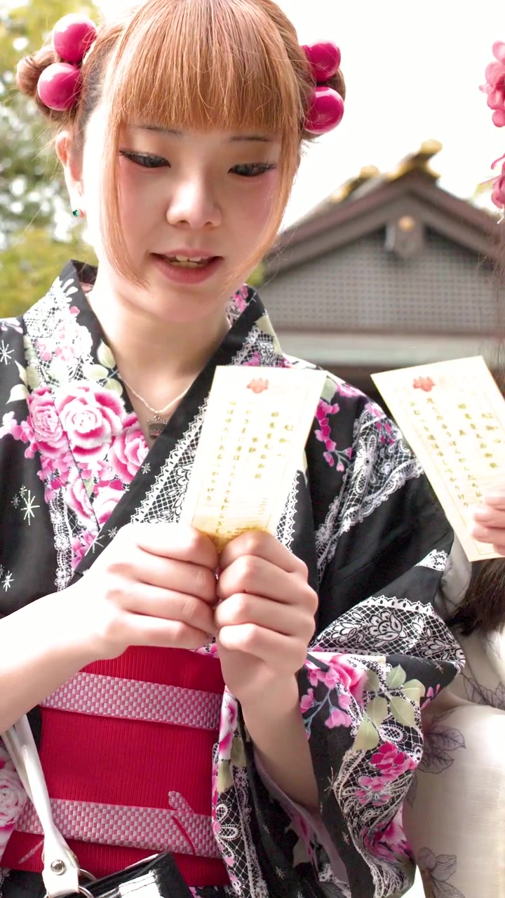 Giovani donne giapponesi in kimono che leggono Omikuji in un tempio