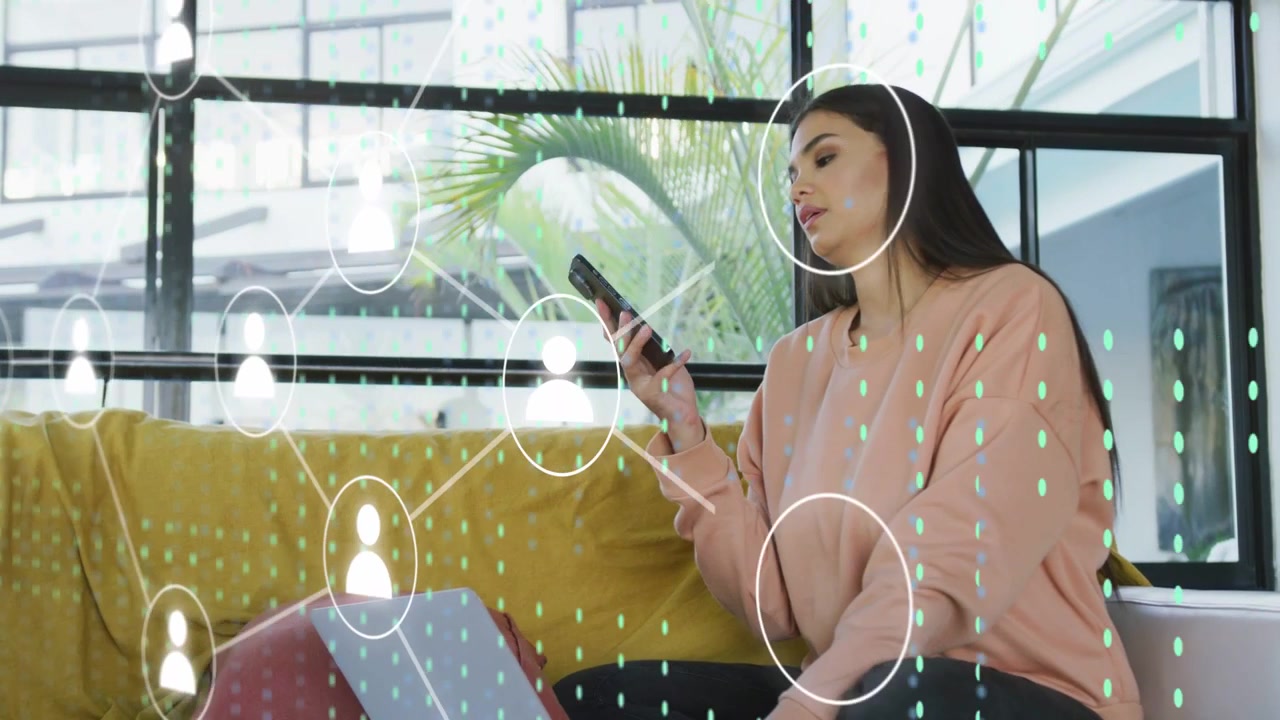 Vertical video: Woman using phone near laptop as net nodes growing, taking call at home in pink top
