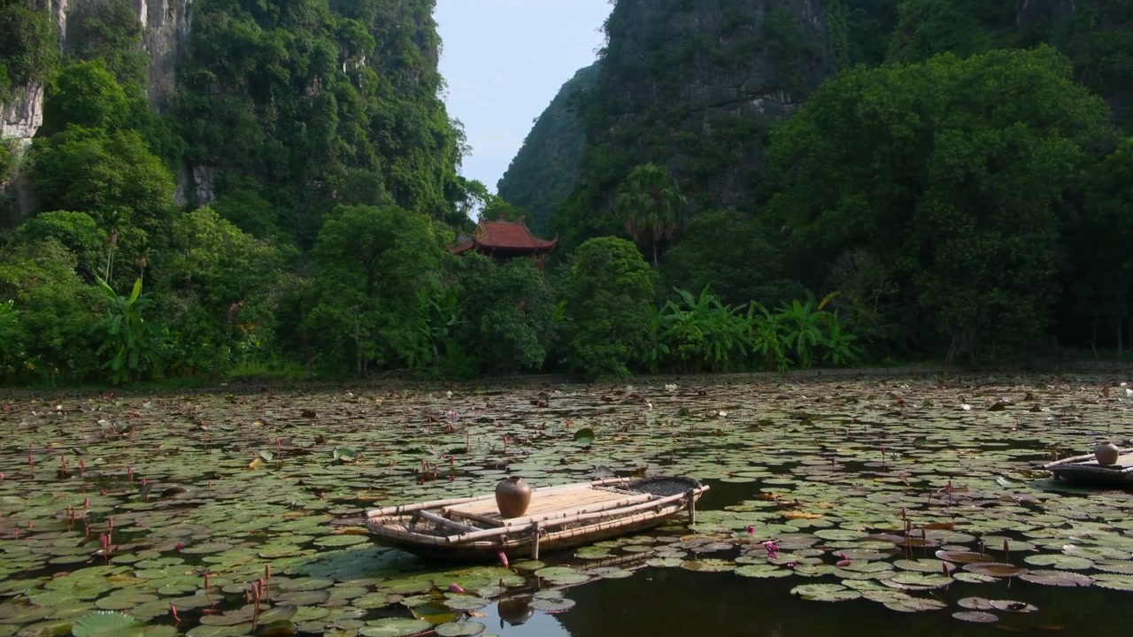 Quang cảnh tuyệt đẹp gần Chùa Bích Động ở Ninh Bình, Việt Nam, với một chiếc thuyền nhỏ và lá sen trên mặt nước cùng những ngọn núi đá vôi xanh tươi ở hậu cảnh.