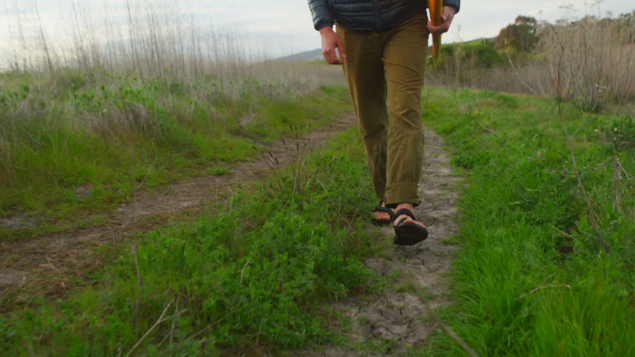 한 서퍼가 보드를 들고 해안 지역의 외딴 서핑 장소로 내려갑니다 1