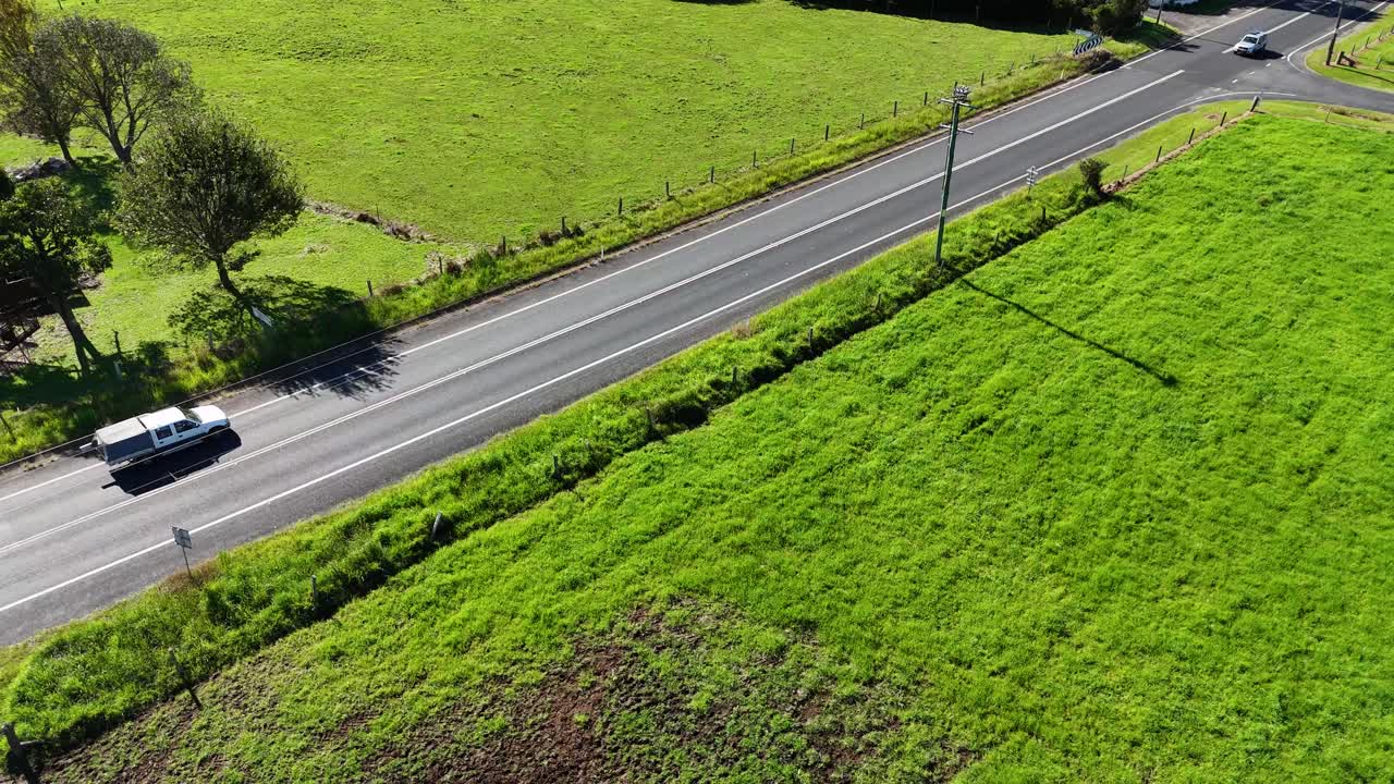 Aerial footage captures vehicles traveling on a rural road surrounded by lush greenery in Dorrigo, NSW, under bright sunlight