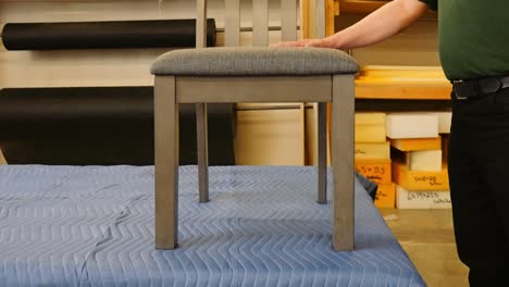 a carpenter walks around a workbench to stand beside a wooden dining chair he built