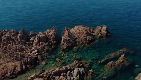 Antena-De-Una-Escénica-Costa-Natural-Playa-Rock-Bay-En-La-Isla-Turística-De-Vacaciones-Cerdeña-En-Italia-Con-Sol,-Azul-Turquesa-Claro-Y-Aguas-Tranquilas-Cerca-De-Capo-Testa