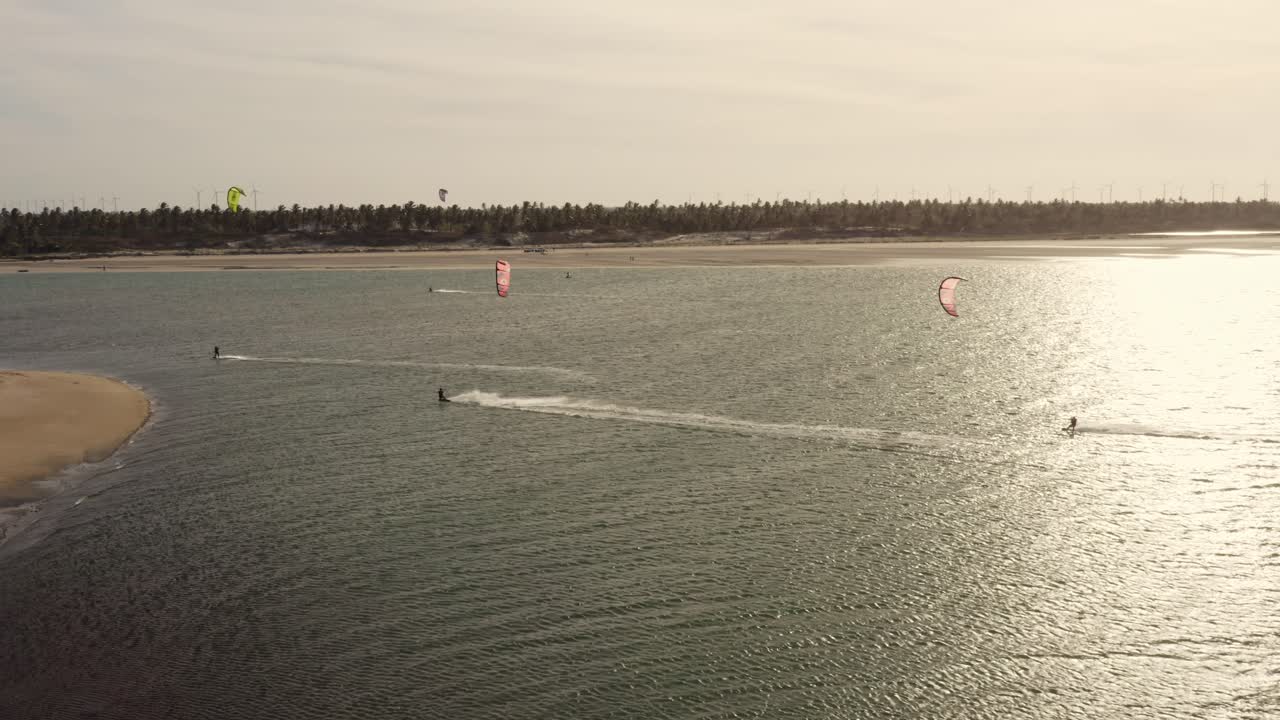 3명의 카이트 서퍼가 일몰 노을 속에서 물결치는 바다에서 항해하고 있습니다.