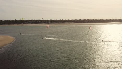 Tres-Kitesurfistas-Navegando-En-La-Ondulación-Del-Océano-En-El-Resplandor-Del-Atardecer