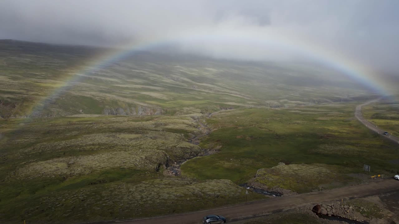 Unveil a surprise rainbow emerging through the fog atop an Icelandic mountain, post-rainstorm &mdash; a mystical moment in crisp 4K, captured by drone