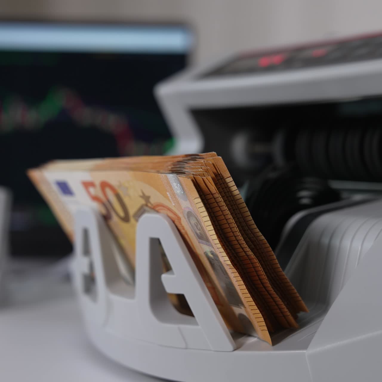 Bargeldverarbeitungsgerät auf dem weißen Tisch. Maschine zählt Fünfzig-Euro-Banknoten. Laptop im Hintergrund