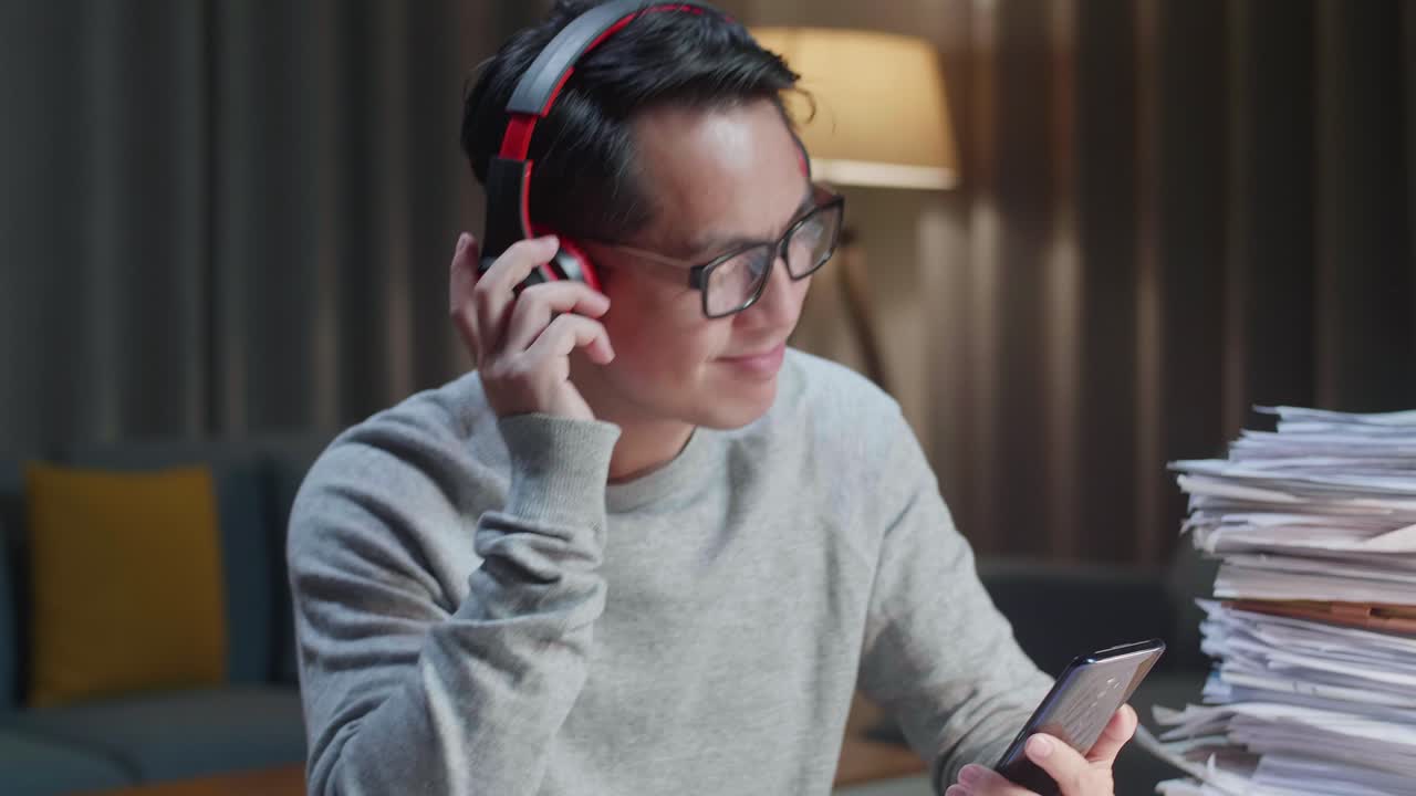 집에서 문서 작업을 한 후 스마트폰에서 음악을 듣는 헤드폰을 가진 아시아 남자의 클로즈업