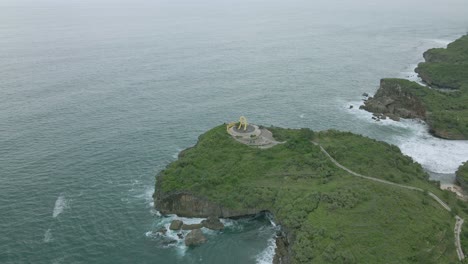 Aerial-shot-of-Fish-Monument-on-Krakal-Beach-in-Indonesia,-surrounded-by-lush-greenery-and-waves