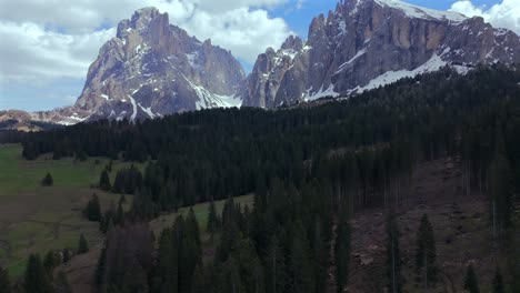 breathtaking aerial view of sassolungo mountain with snow-capped peaks and dense pine forests in the dolomites, showcasing a beautiful alpine landscape