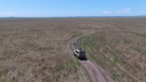 drone shot of off-road vehicle drives through grasslands in serengeti