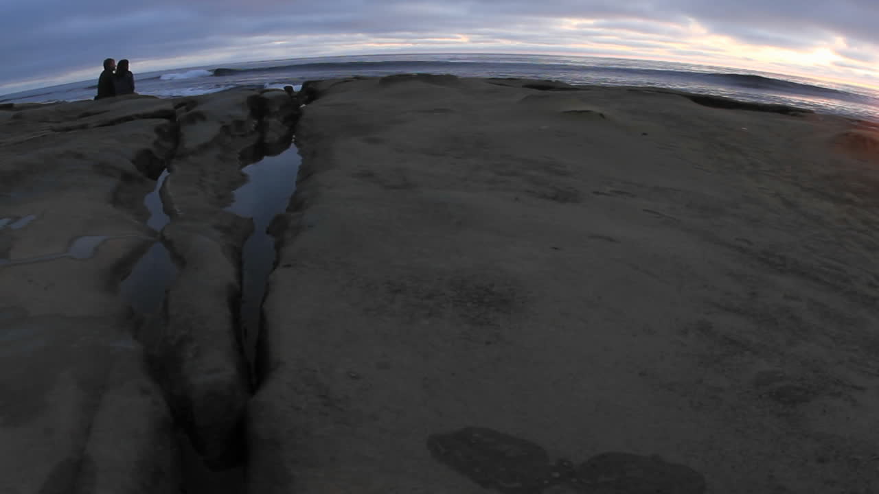 una vista de ojo de pez de una pareja viendo las olas rodar en una playa justo después del atardecer