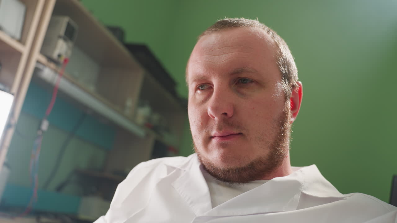 una vista de cerca de un técnico en una bata de laboratorio, profundamente en pensamiento mientras está sentado en un entorno de laboratorio