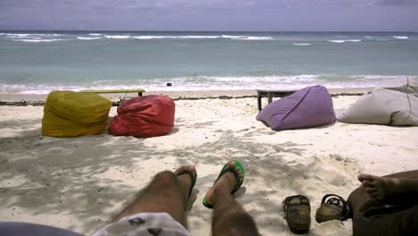 An-Einem-Sonnigen,-Windigen-Tag-Liegt-Ein-Mann-Am-Strand-Auf-Einem-Sitzsack-Im-Schatten-Der-Bäume