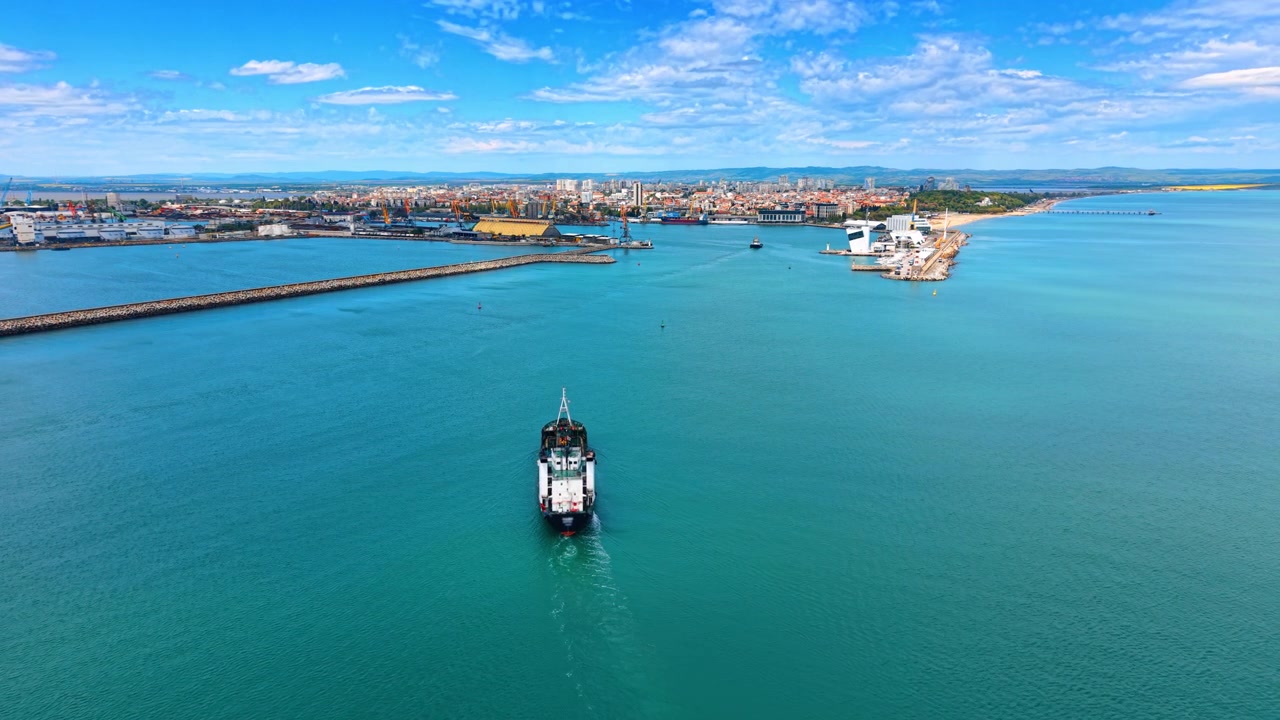 Vista aerea di una nave cisterna che naviga all'ingresso del canale portuale. Prospettiva da drone di una grande nave da carico che naviga lungo un canale portuale verso una città portuale con frangiflutti.