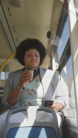 vertical video of plus size biracial woman drinking coffee and using smartphone in bus