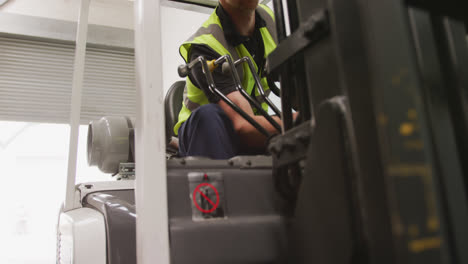 Caucasian-male-factory-worker-at-a-factory-with-a-hat-and-high-vis-vest,-using-a-truck