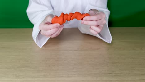 las manos manipulan arcilla naranja en una mesa
