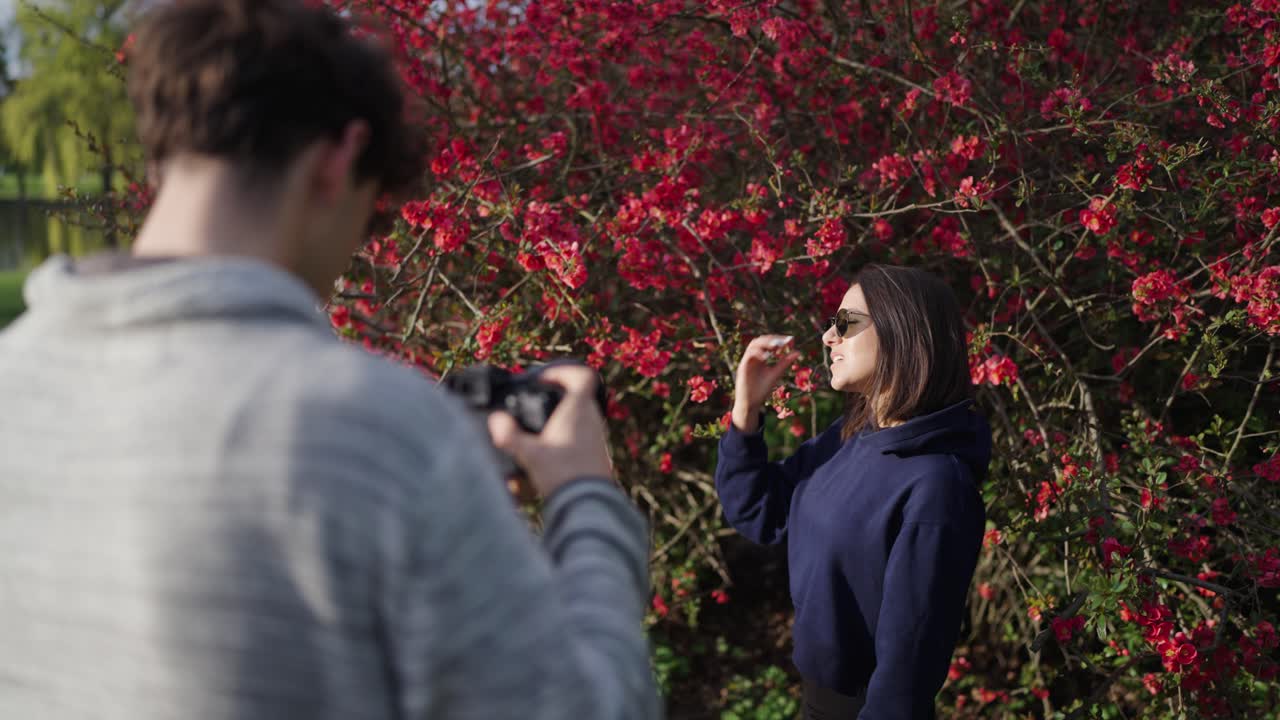 Fotógrafo com câmera digital faz ensaio fotográfico com mulher perto de arbusto florido
