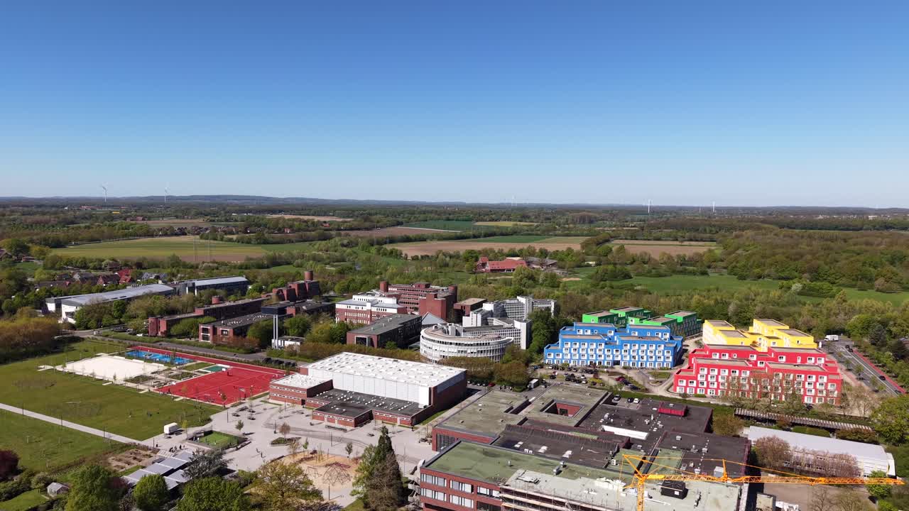 Campus universitario suburbano americano in primavera con edifici colorati, campi sportivi, alberi e quartieri vicini sotto un cielo sereno e soleggiato. Edifici in mattoni rossi e dormitorio multicolore. Ripresa aerea in ascesa.