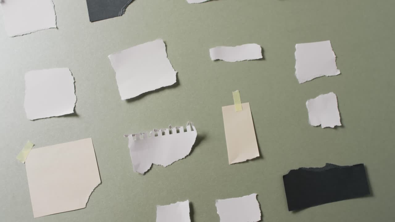 Video of close up of multiple torn pieces of paper on green background