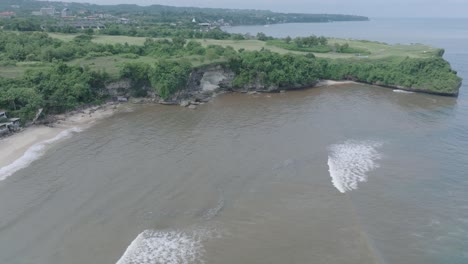 Panning-down-aerial-drone-shot-over-polluted-muddy-water-and-floating-trash-and-debris-mixing-with-turquoise-water-and-tropical-coastine-in-Bali-Indonesia