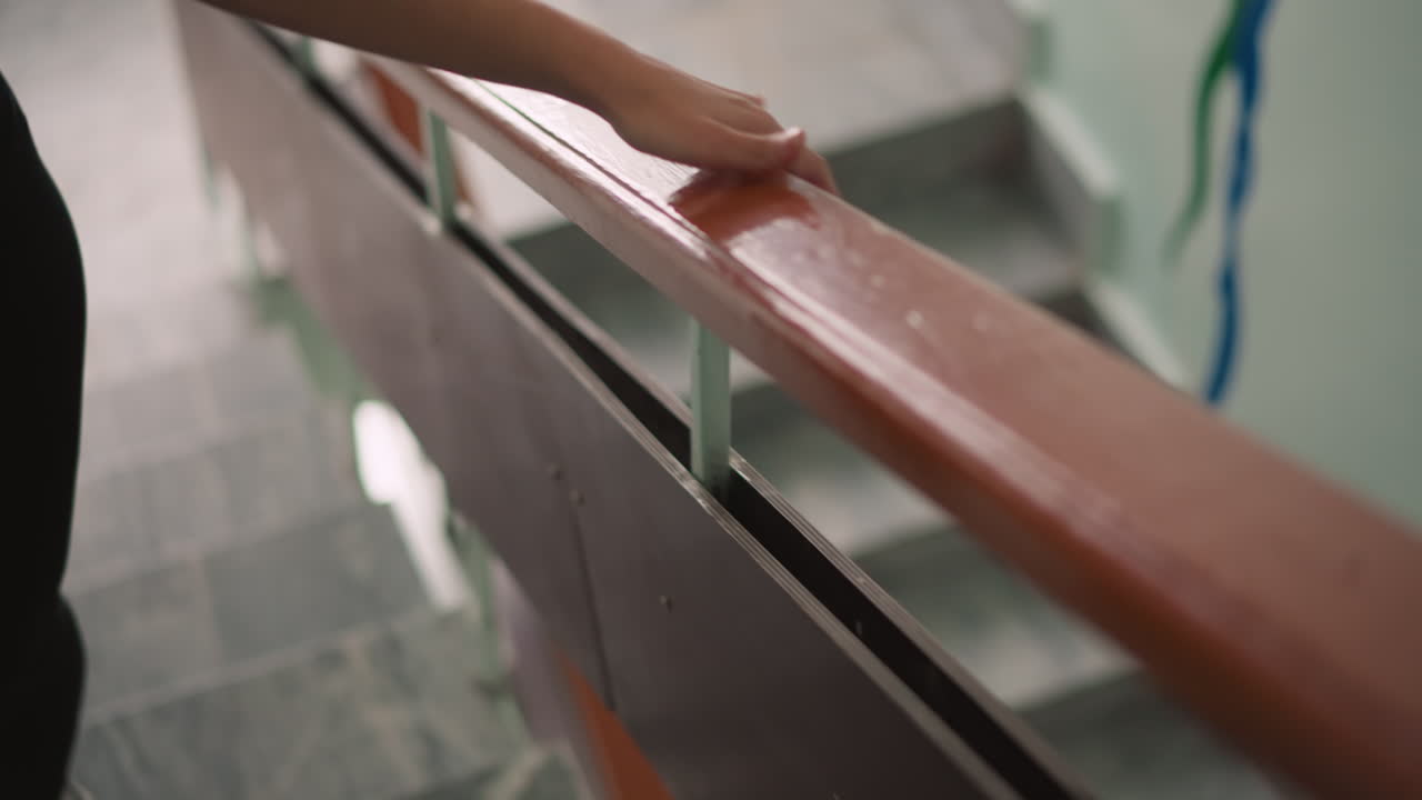 Side view of girl in black leggings climbing staircase with hand moving along glossy handrail, steady upward motion indoors showing detail of support, balance, casual lifestyle and everyday activity
