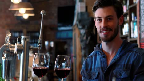 retrato de un barman sosteniendo dos vasos de vino tinto en el mostrador de la barra