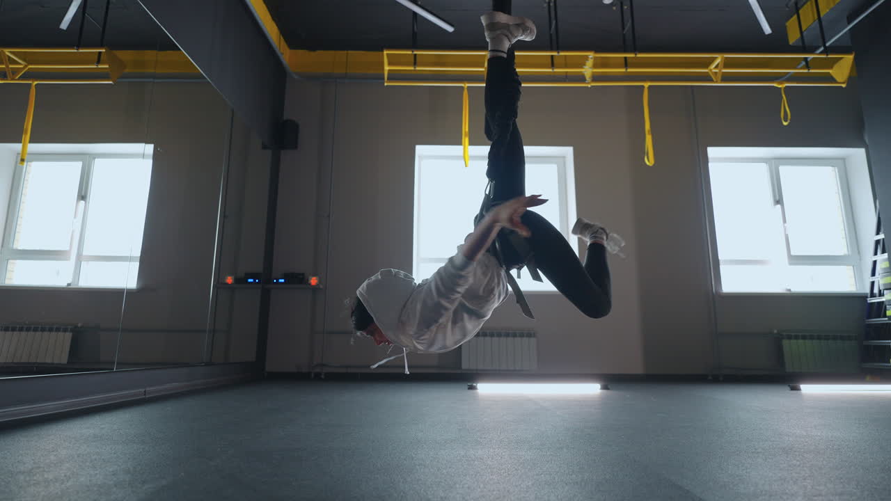 ejercicio acrobático en el sistema trx en el gimnasio joven mujer atlética está colgando con la cabeza hacia abajo y girando