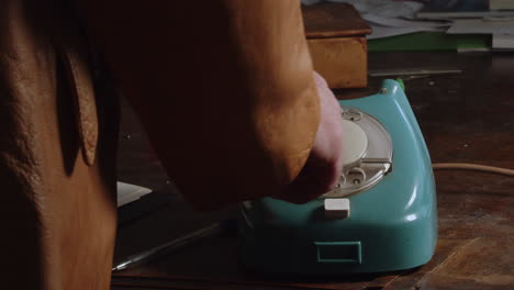 the person in the leather jacket picks up the handset and dials a number on the phone