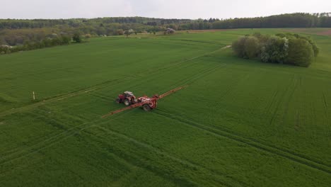 Aerial-circular-drone-footage-of-a-tractor-spraying-a-huge-green-meadow-with-water-or-pesticide-with-its-sprinkler-system