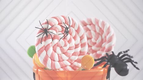 arañas cayendo en un cubo de calabaza de halloween lleno de dulces contra cuadrados concéntricos