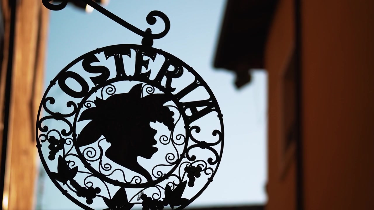 Insegna stradale decorativa in metallo per esterni con silhouette di Bacco appesa fuori da una tradizionale osteria italiana