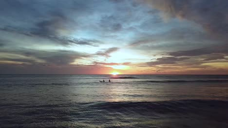 Drone-shot-of-waves-and-surfers-in-Aruba,-Caribbean-with-spectacular-sunset