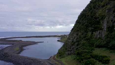drone boom view revelando un pueblo costero, exuberante paisaje de acantilados verdes, laguna, fajã de santo cristo, isla de são jorge, las azores, portugal