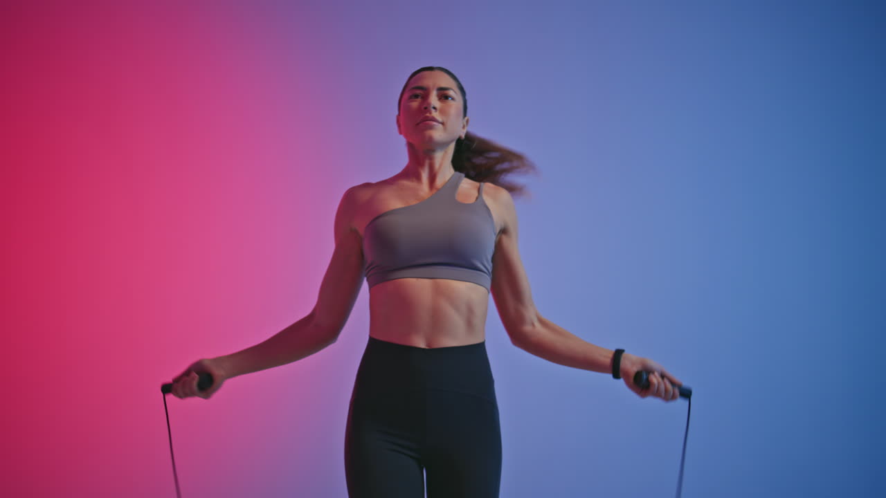 Serious fitness woman jumping in neon club. Female athlete using skipping rope