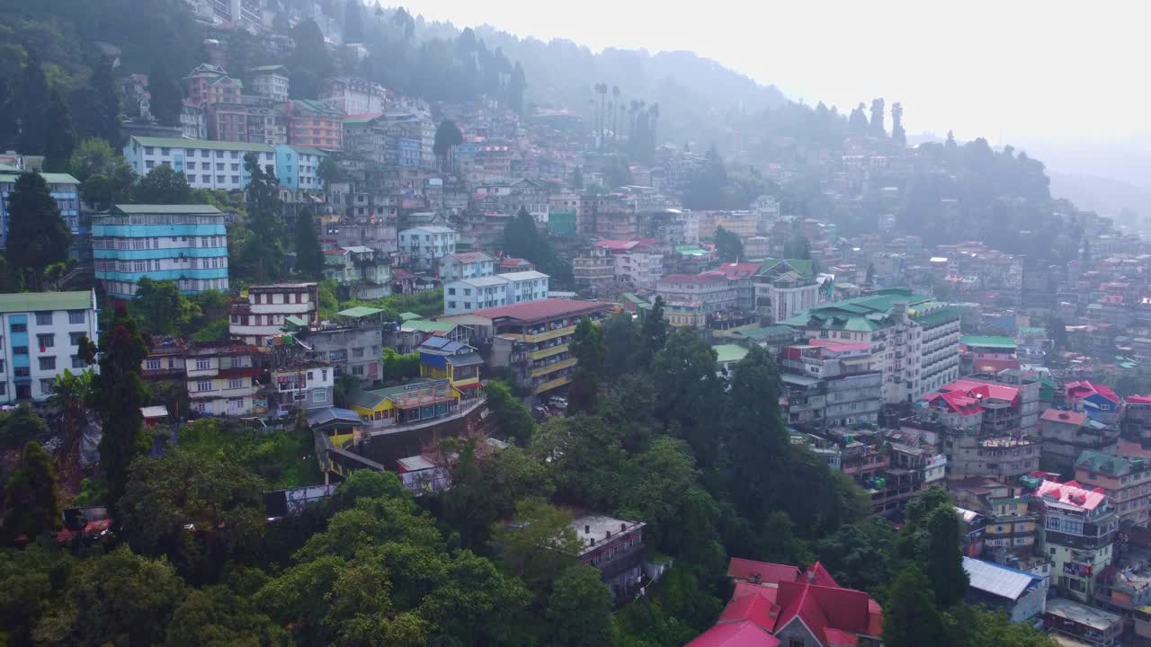 Dron latający nad domami mieszkalnymi na wzgórzu, komercyjnymi hotelami i budynkami restauracyjnymi w mieście Darjeeling zimą, przy historycznej drodze górskiej w Bengalu Zachodnim. Ujęcie wprowadzające.