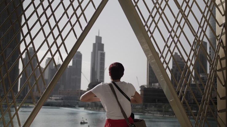 Une femme se tient sur un balcon, regardant la ville de Dubaï avec de grands immeubles et des gratte-ciel au loin.