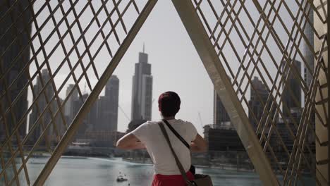 una mujer se para en un balcón mirando la ciudad de dubai con grandes edificios y rascacielos en la distancia