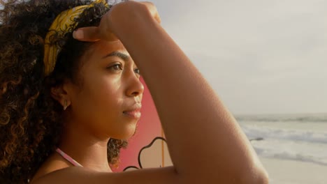 vista lateral de una surfista afroamericana de pie con una tabla de surf en la playa 4k