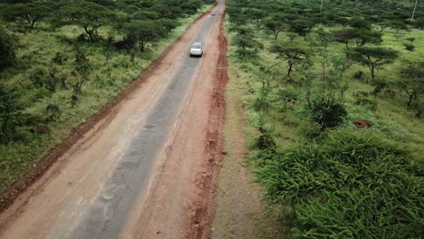 Luftaufnahme-Eines-Weißen-4x4-Autos,-Das-Frontal-Entlang-Einer-Schmutzigen-Und-Trockenen-Straße-Kommt,-Die-Von-Grüner-Savanne-Umgeben-Ist