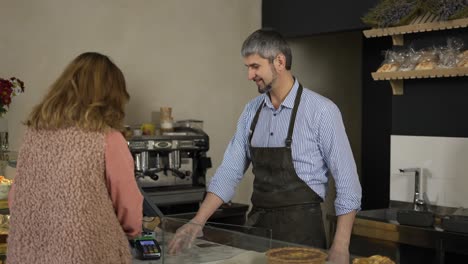 handsome male cashier in apron and gloves accepts terminal payment from female customer