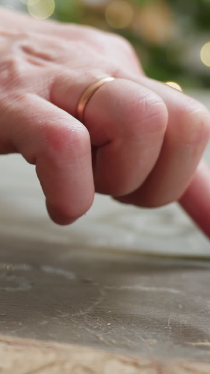 closeup white hand drawing heart on dusty tabletop with bokeh lights and evergreen background, fingertip traces delicate heart shapes with gold glitter flecks, ring visible frames suggest