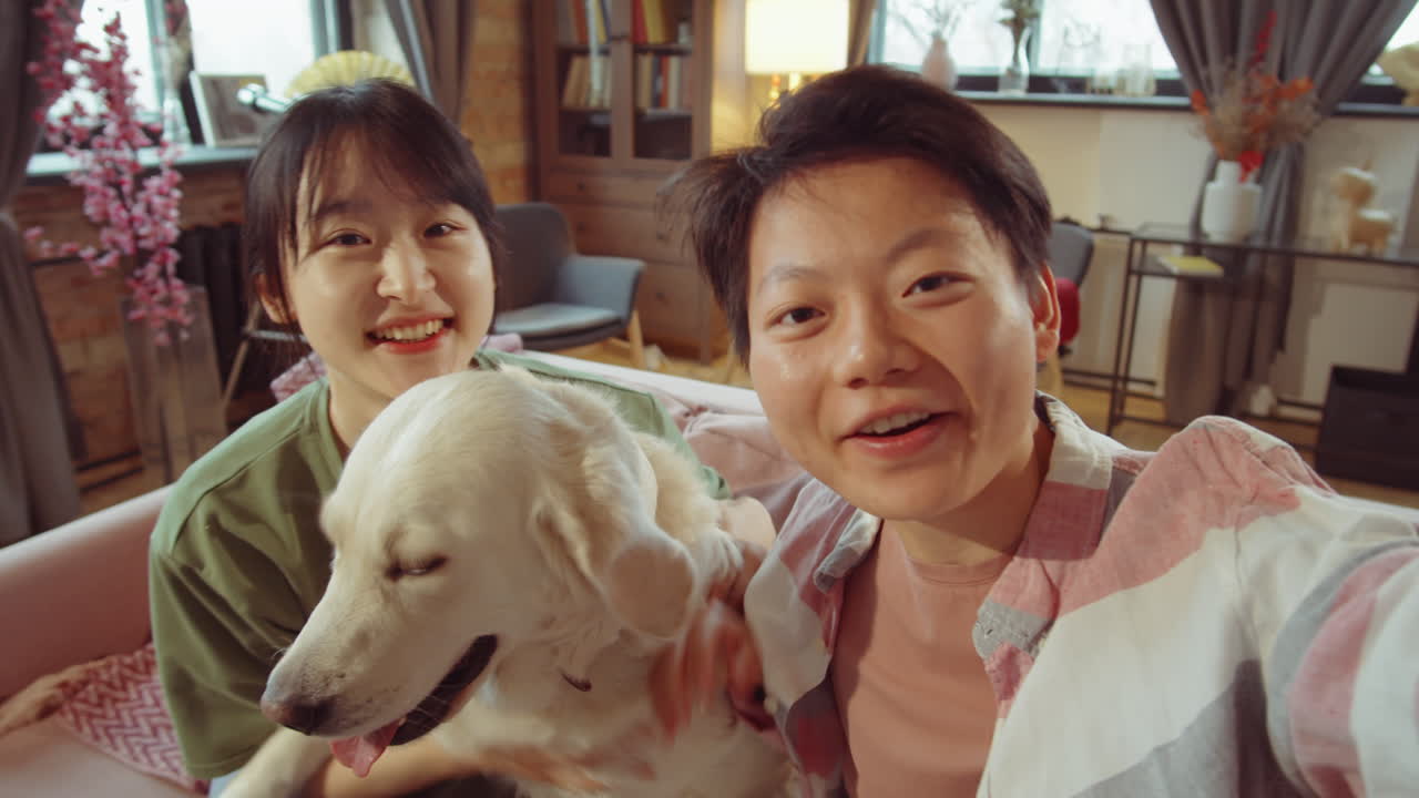개와 함께 앉아서 비디오 통화로 대화하는 즐거운 아시아 여자 친구들