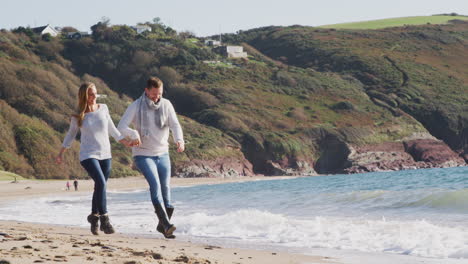 couple running through waves on winter beach vacation