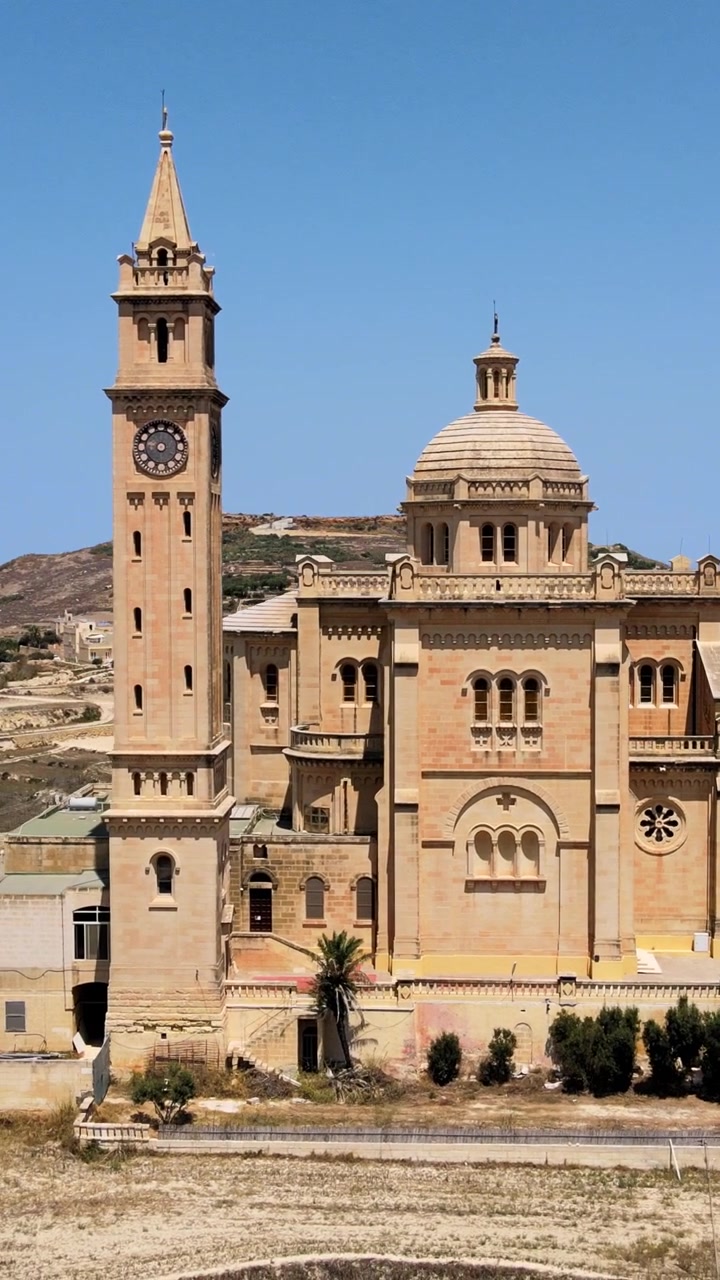 Splendido filmato verticale con drone della Basilica di Ta' Pinu a Gozo, Malta. Luce mediterranea brillante, cieli azzurri e architettura elegante. Ideale per i social media.
