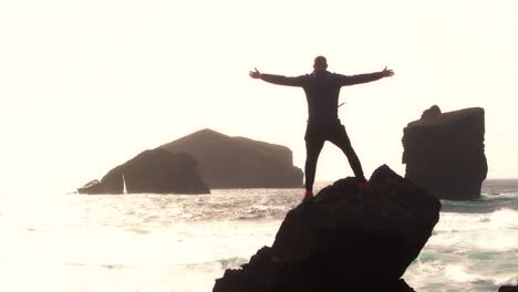 silhouette of man standing at the beach over a rock with open arms