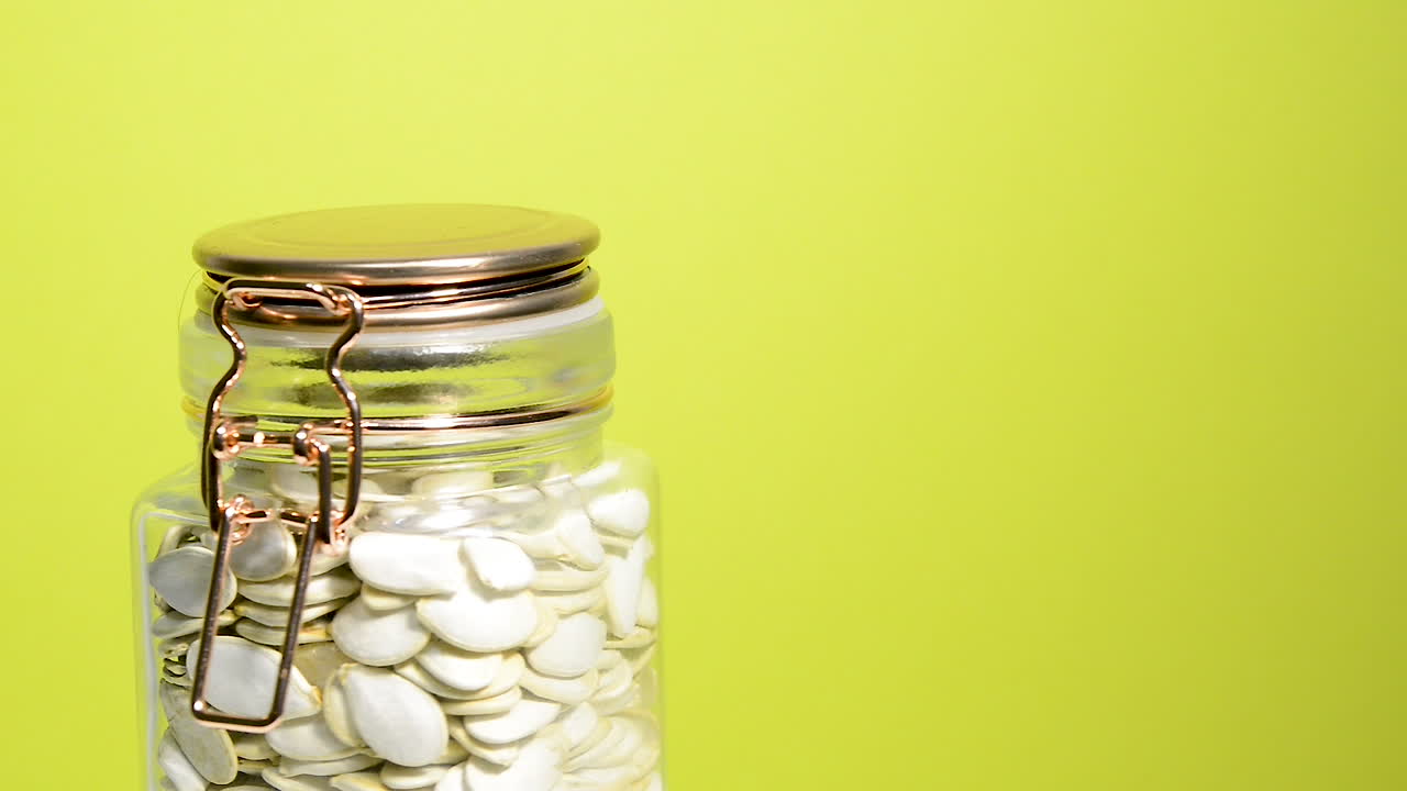 네온 노란색 배경에 호박씨와 함께 회전하는 밀폐된 메이슨 항아리의 세부 사항